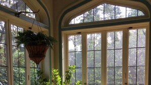 A sunlit room with large windows, wicker furniture, and hanging plants.