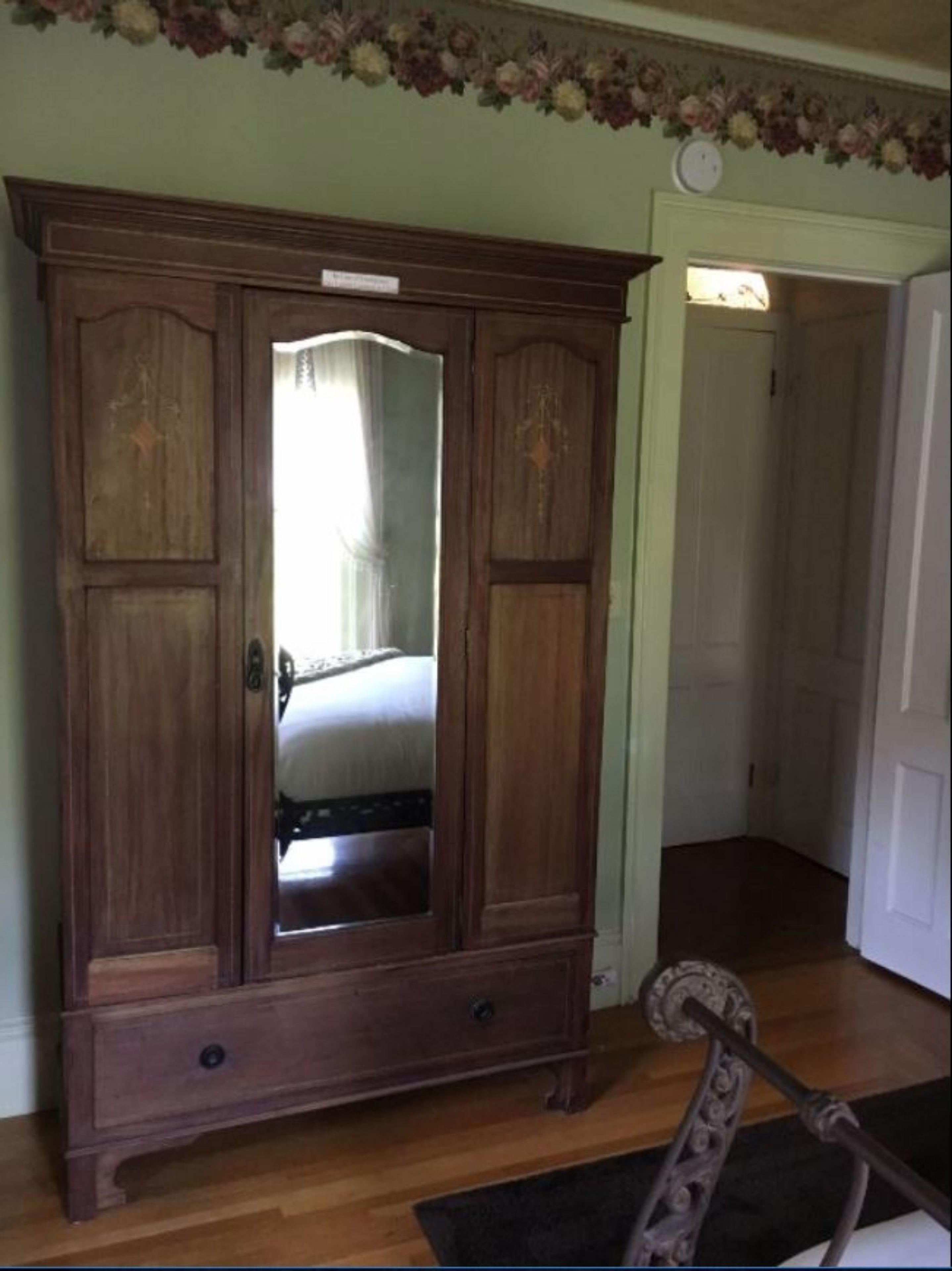 A wooden wardrobe with a mirror, a small drawer, and a door.