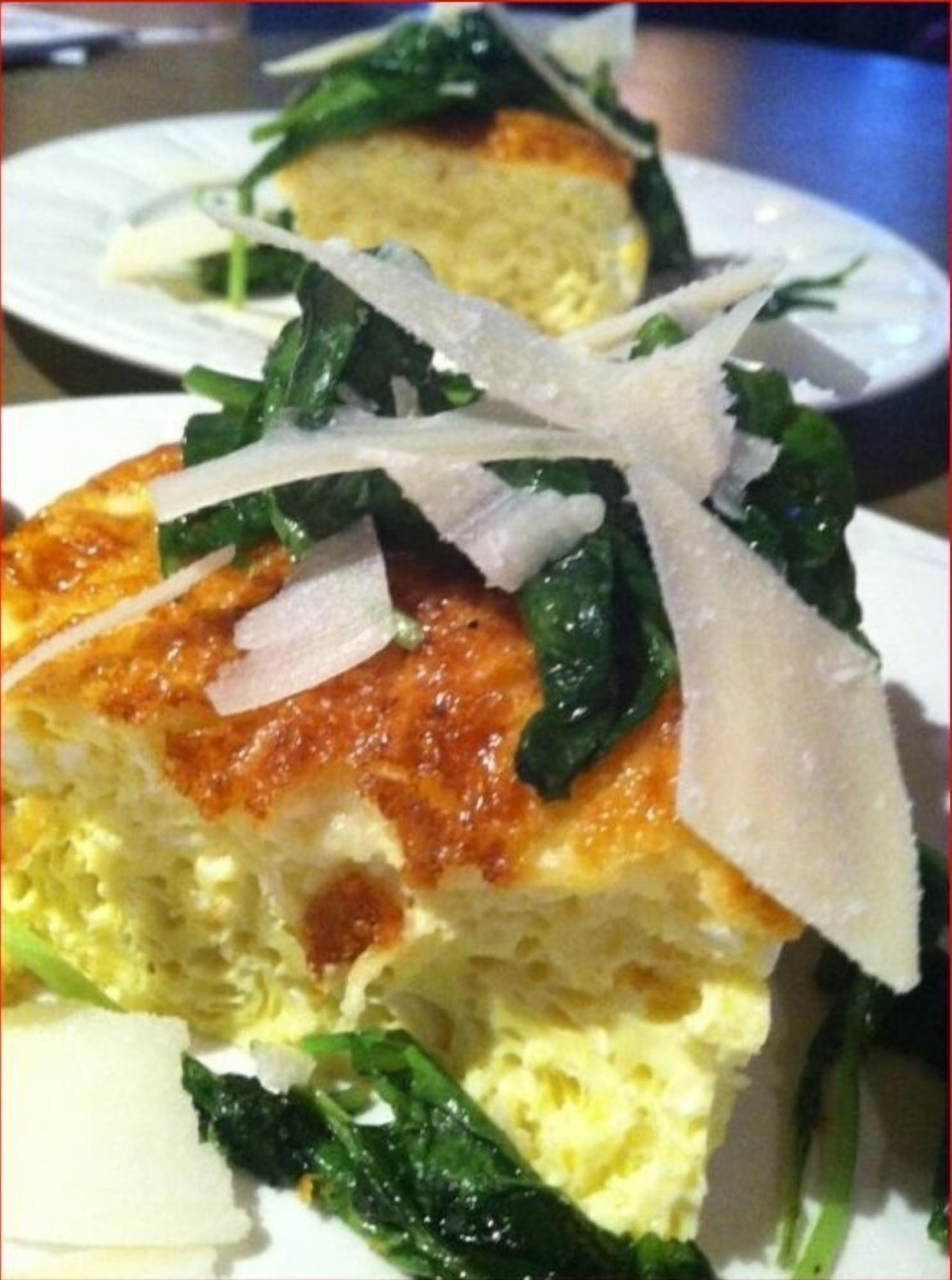 A slice of quiche with spinach and cheese on a white plate.