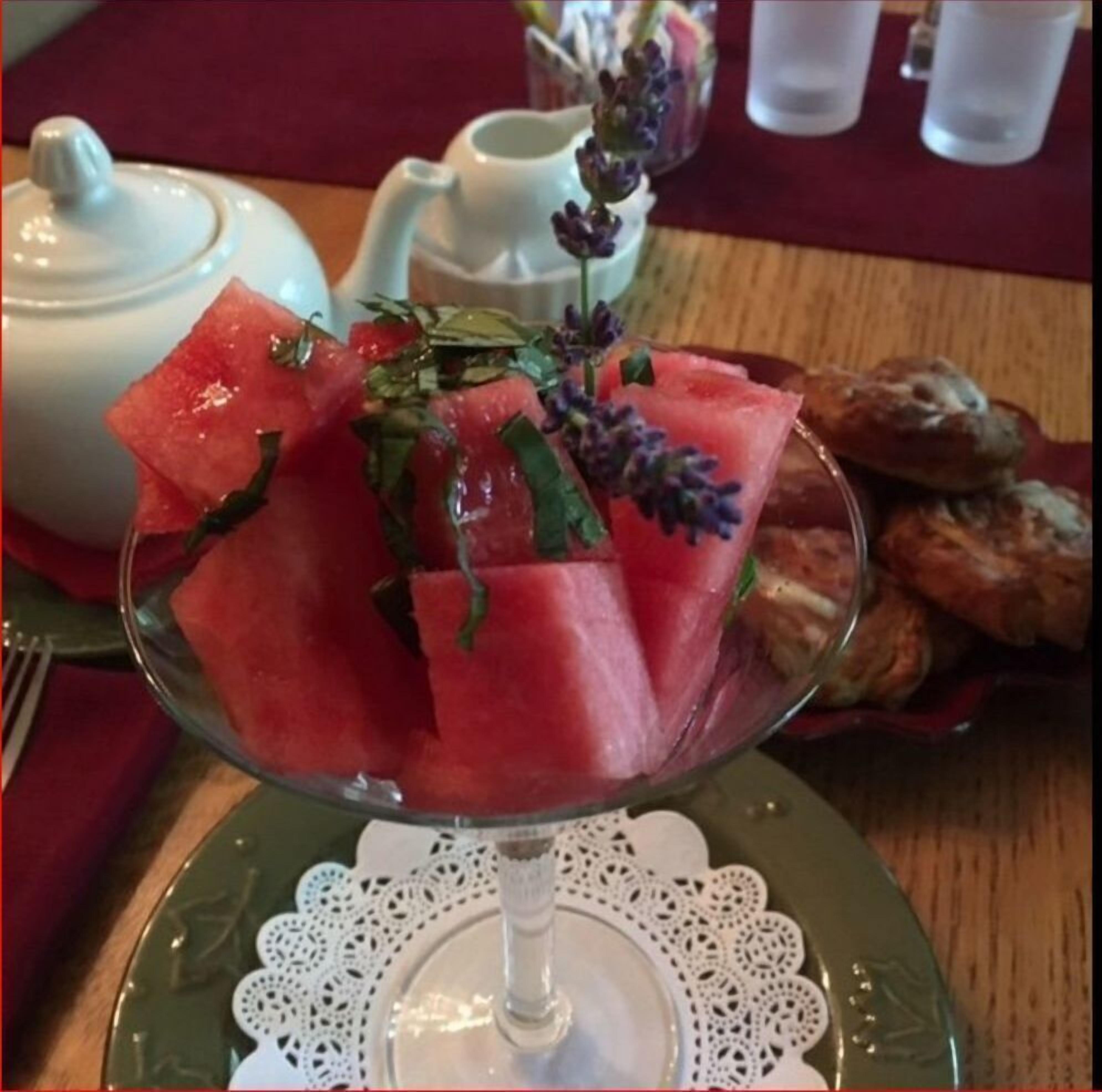 A dessert plate with watermelon slices and lavender on a table with a teapot and cups.