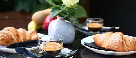 A table setting with croissants, a cup of coffee, and a vase with a flower.