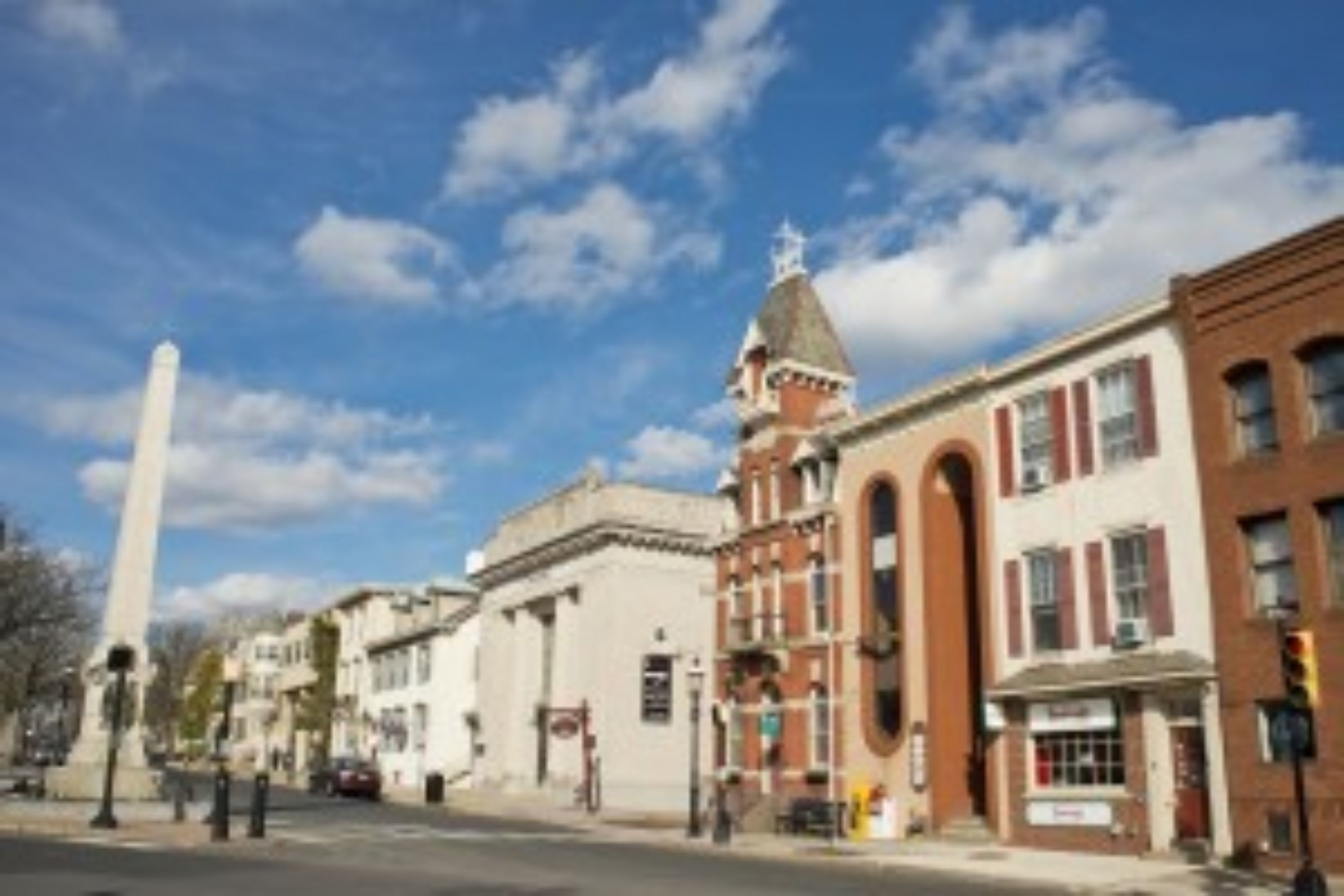 A street view with historic buildings, a prominent monument, and a clear sky.