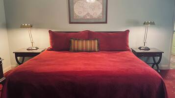 A neatly made bed with a red quilt, two bedside lamps, and a framed map on the wall.