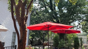 An outdoor patio with brick flooring, metal chairs, a red umbrella, and a tree. - Hargrave House B & B (Doylestown)