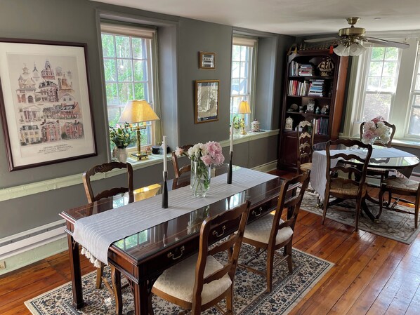 A dining area with a wooden table, chairs, and a chandelier. There are bookshelves and a framed picture on the wall.