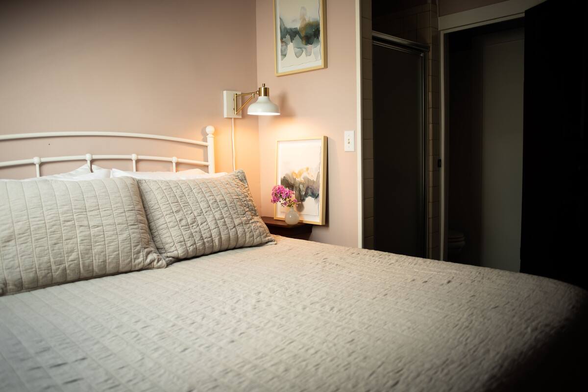 A neatly made bed with a quilted blanket and pillows, a bedside lamp, and a framed picture on the wall.