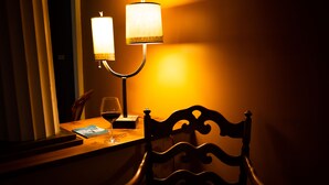 Une pièce faiblement éclairée, avec une table en bois, une chaise, un verre à vin et une lampe.
