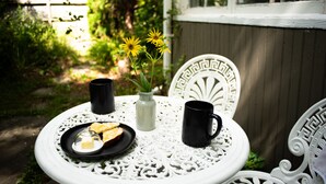 Une table blanche, placée à l’extérieur, agrémentée d’un vase décoratif, de deux tasses noires et d’une assiette contenant de la nourriture.