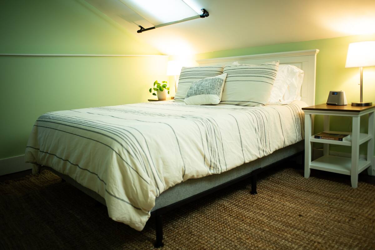 A neatly made bed with a striped bedspread, a bedside lamp, and a small nightstand with a book.