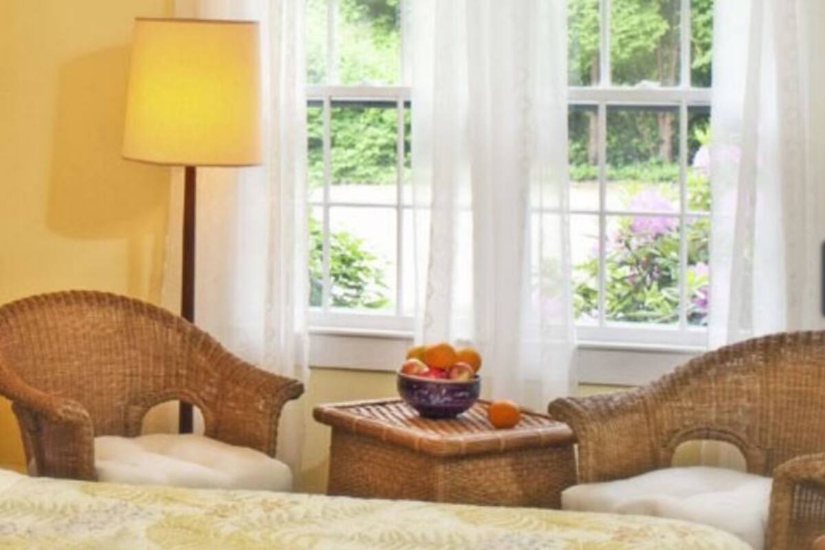 A room with wicker chairs, a small table with a bowl of fruit, and a window with curtains.