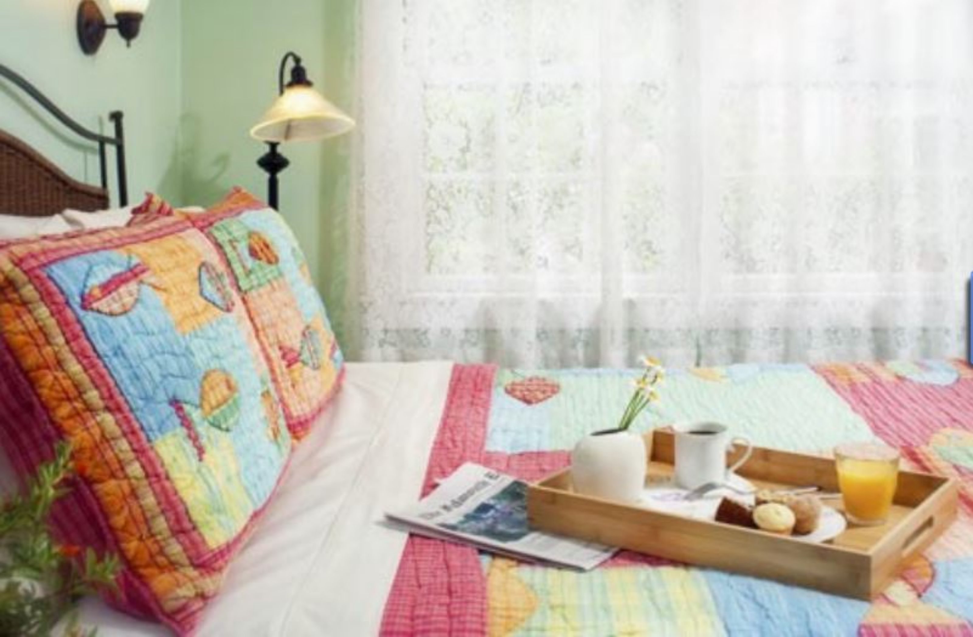 A bed with a colorful quilt, a tray with breakfast items, and a lamp.