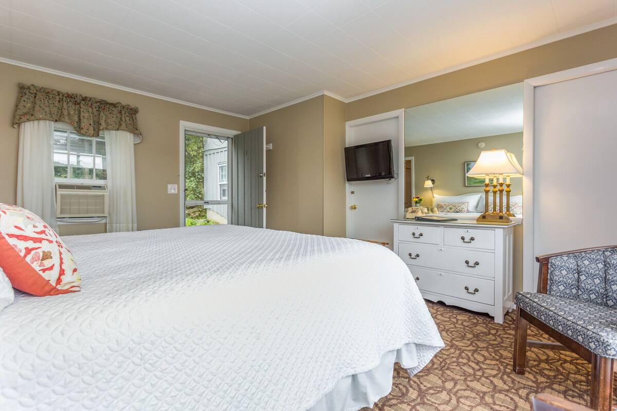 A bedroom with a large bed, a dresser, a chair, a television, and a window with curtains.