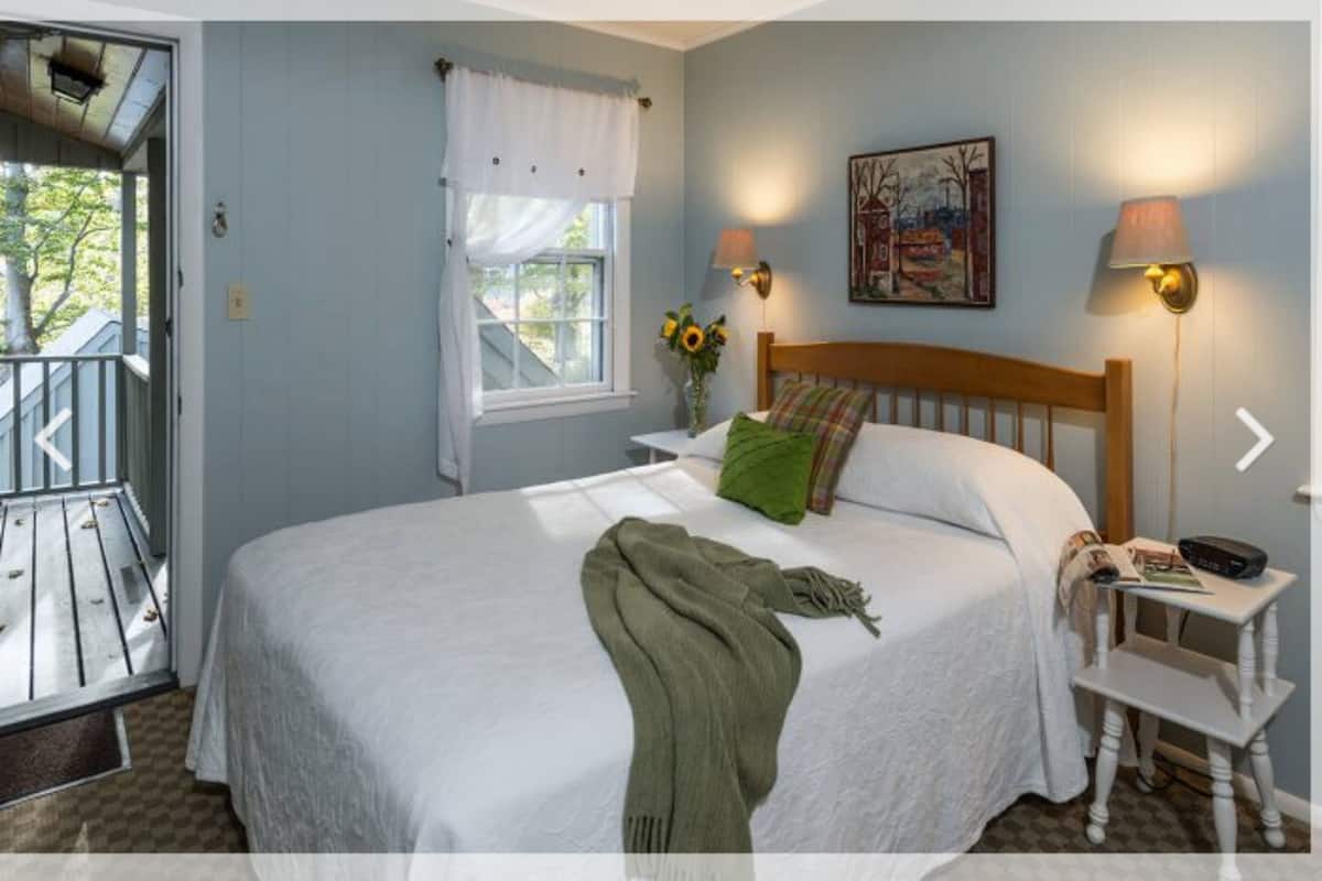 A bedroom with a bed, nightstands, a window with curtains, a painting, and a lamp.