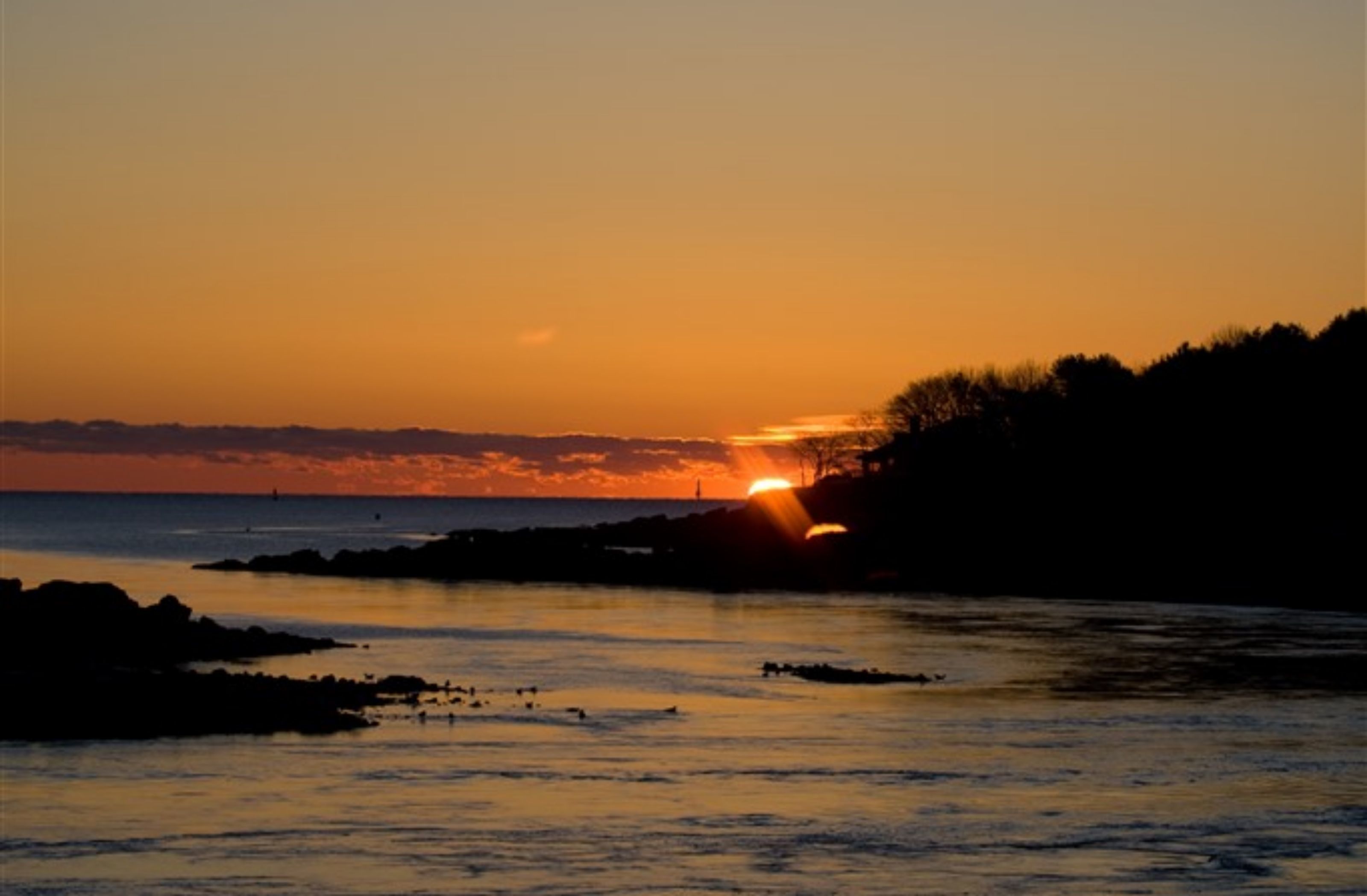 A sunset over a coastal area with rocky shores and calm waters.