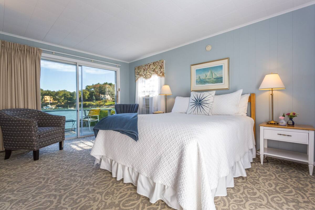 A hotel room with a large bed, a chair, a nightstand, and a view of the sea.