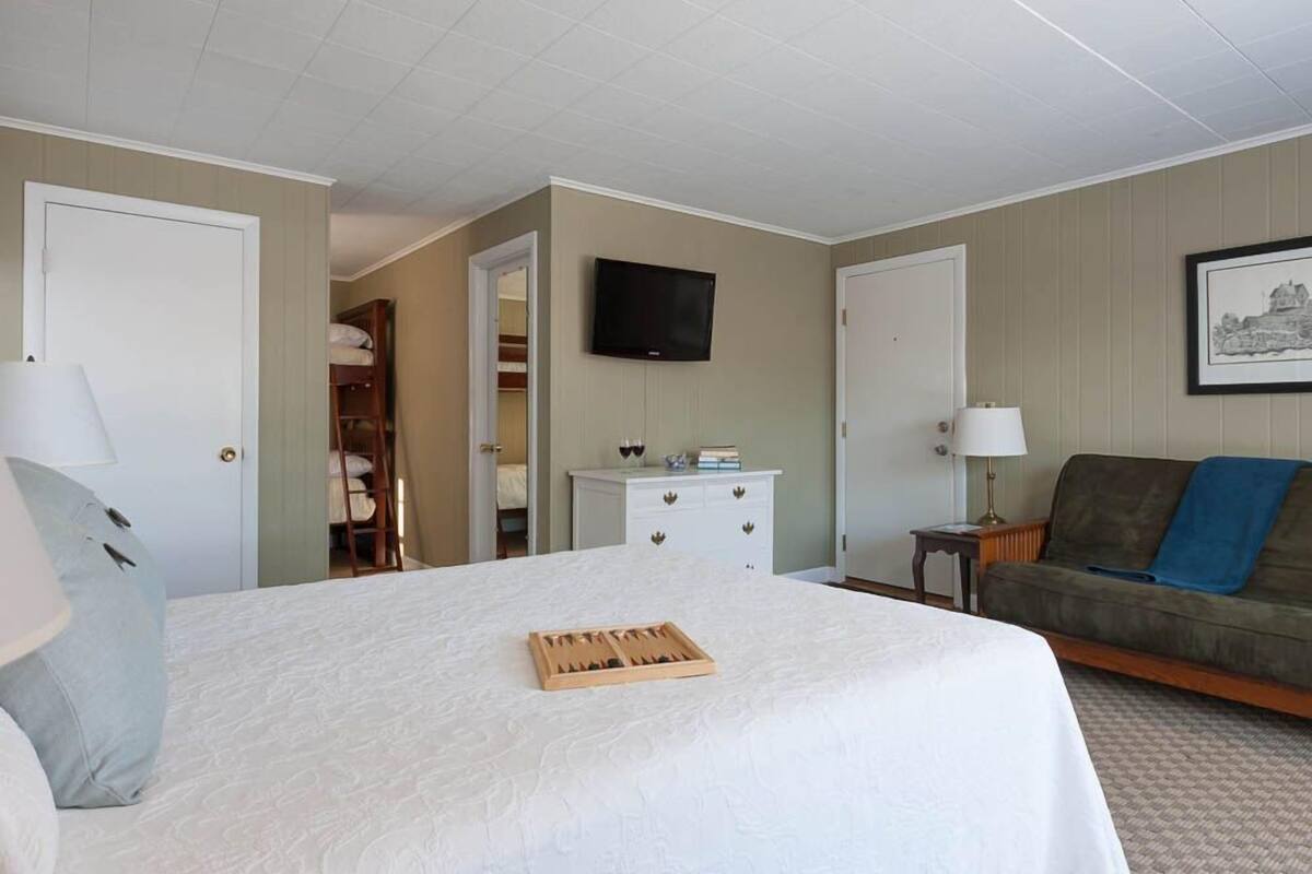 A hotel room with a large bed, a television mounted on the wall, a sofa, and a small table with a lamp.