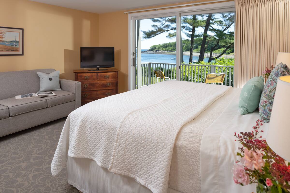 A bedroom with a bed, a television, a sofa, and a balcony with a view of the sea.