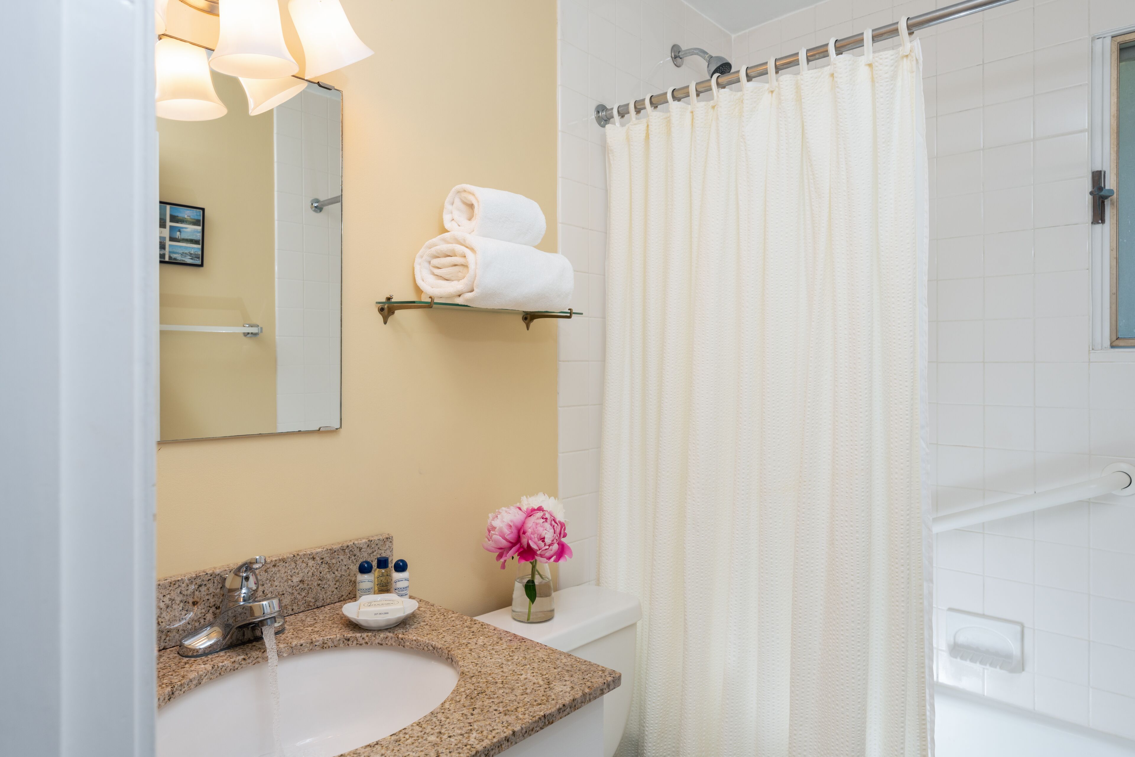 A bathroom with a sink, mirror, towel rack, shower curtain, and a vase with flowers.