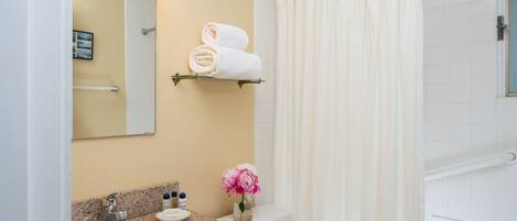A bathroom with a sink, mirror, towel rack, shower curtain, and a vase with flowers.