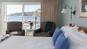A hotel room with a large bed, two armchairs, a nightstand, a lamp, and a view of the sea. - Dockside Guest Quarters & Restaurant (York)