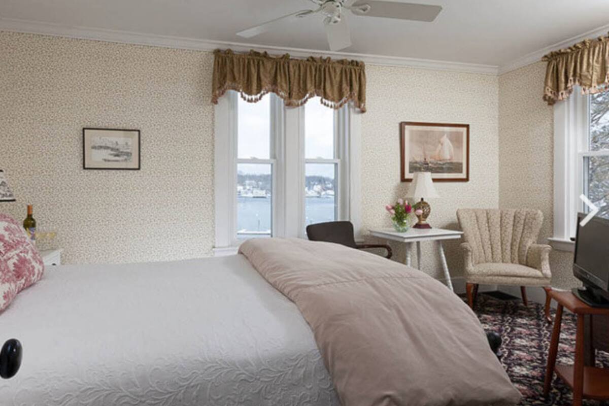 A hotel room with a large bed, a desk with a chair, a television, and two windows with curtains.