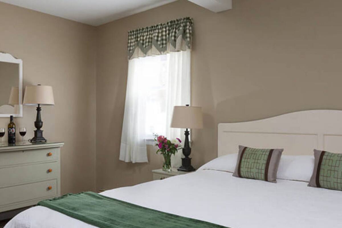 A hotel room with a bed, two bedside tables with lamps, a dresser, and a window with curtains.