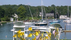 A marina with boats docked, a grassy area with white chairs, and a forested background. - Dockside Guest Quarters & Restaurant (York)