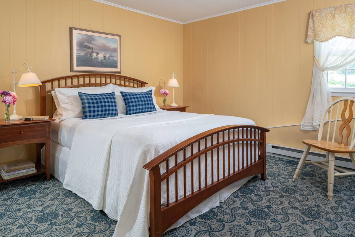 A neatly arranged bedroom with a wooden bed, two bedside tables with lamps, a chair, and a framed picture on the wall.
