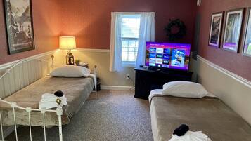 A room with two beds, a TV, a window with curtains, and a wall with framed pictures.