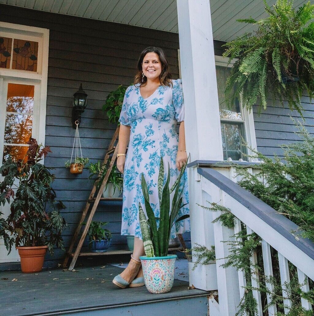 Une véranda où se tient une femme, entourée de plantes en pot et d’une échelle en bois.