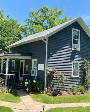 A two-story house with a porch, a small garden with flowers, and a clear blue sky.