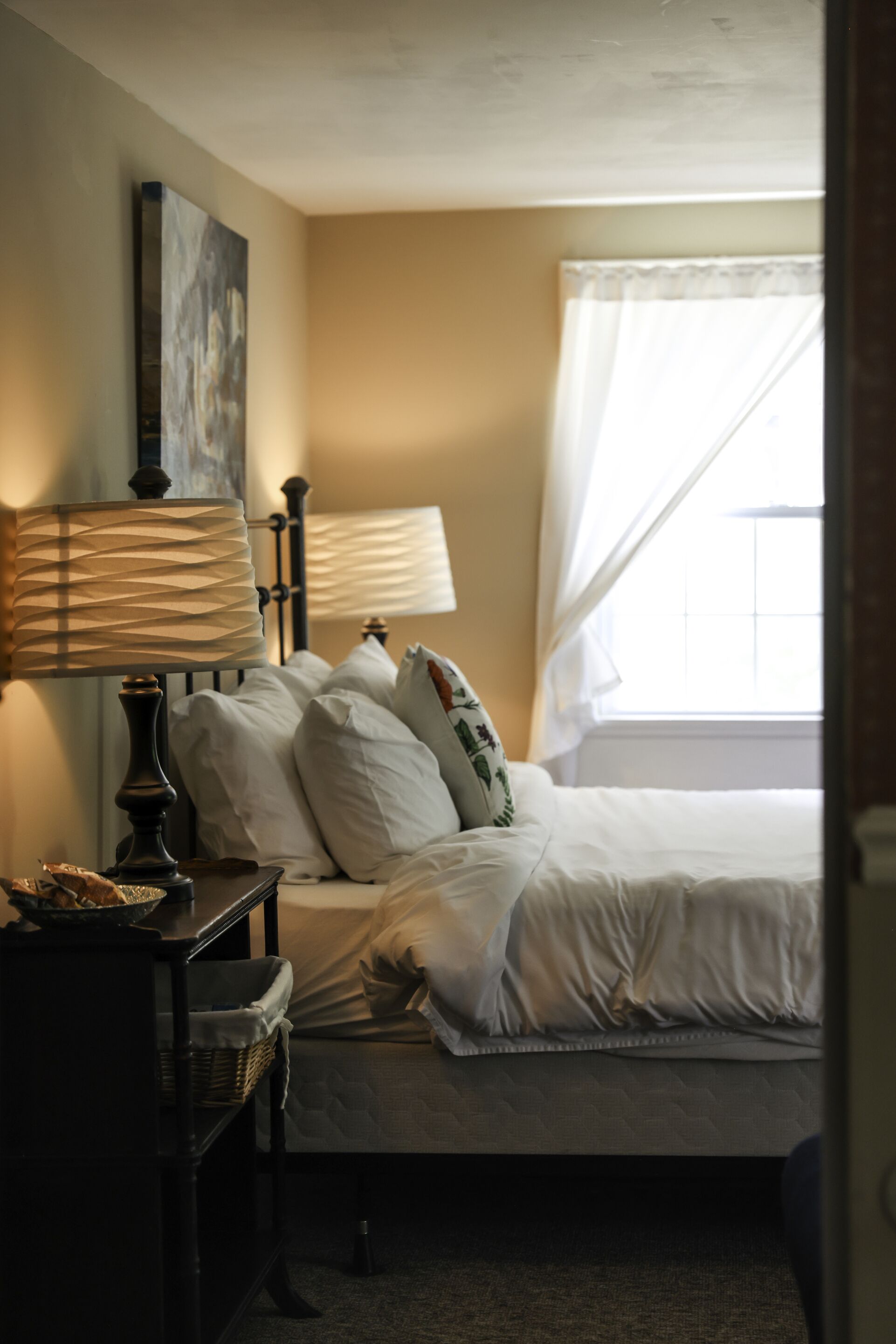 A bedroom with a bed, a nightstand, a lamp, and a window with curtains.