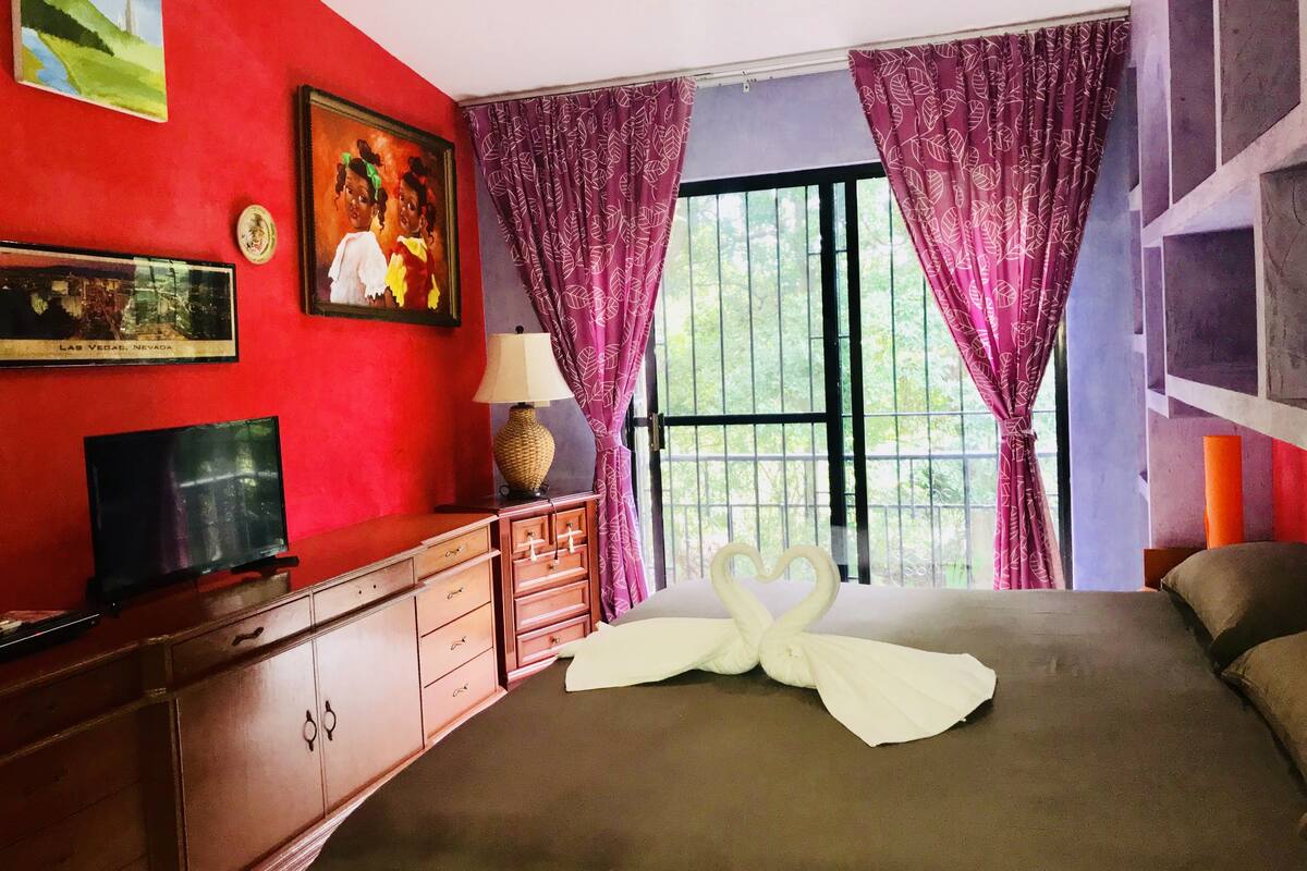 A hotel room with a bed, a TV, a dresser, and a window with curtains.