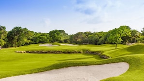 Un campo de golf con búnkeres de arena, césped verde y exuberante, y árboles al fondo.