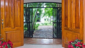 Una puerta de madera que da a un jardín con un sendero empedrado y palmeras.
