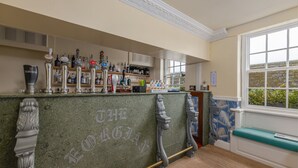 A bar area with multiple taps, shelves of bottles, and a view of greenery through a window. - Georgian House Hotel (Whitehaven)