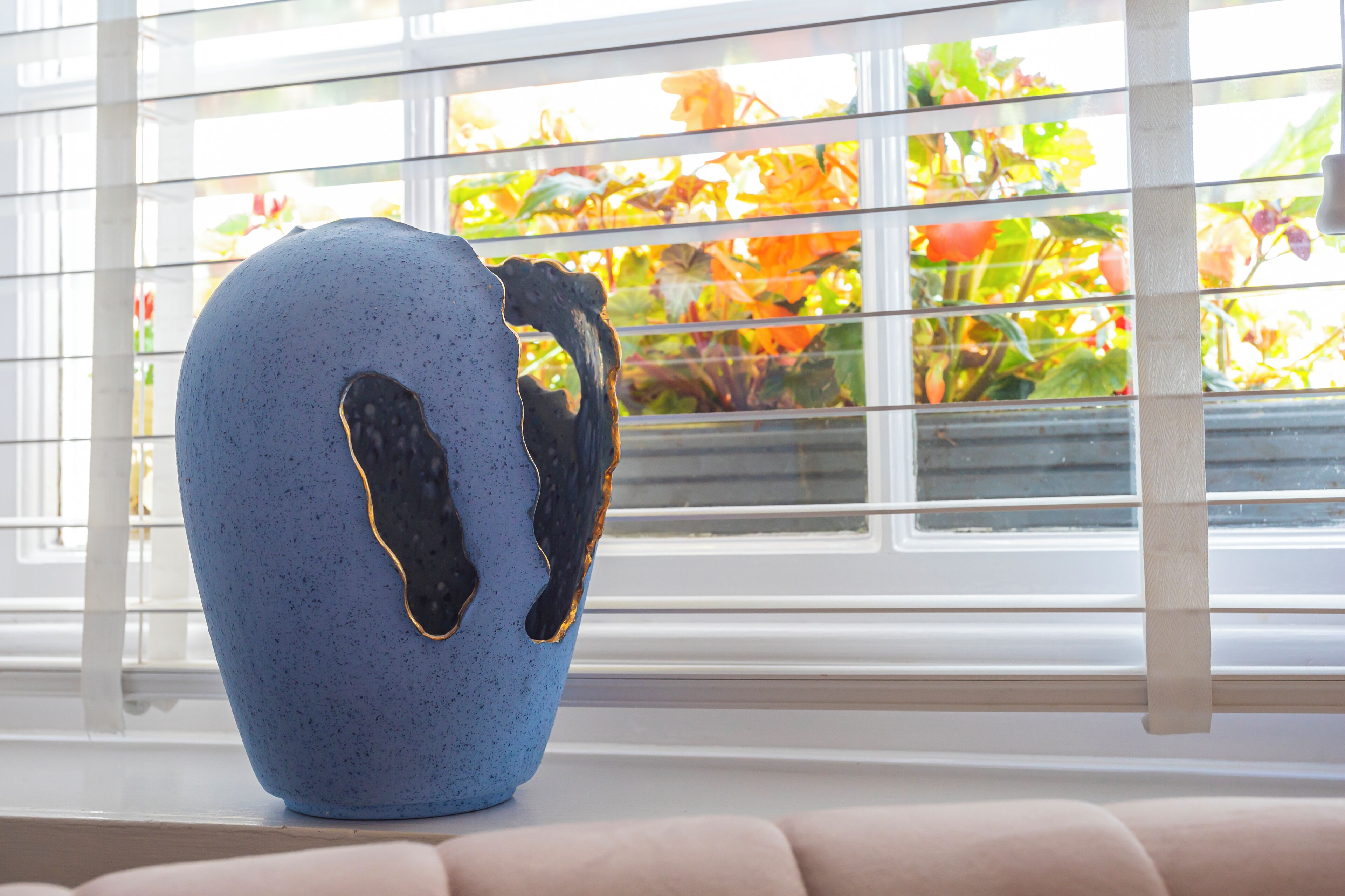 A blue ceramic vase with a gold rim on a windowsill.