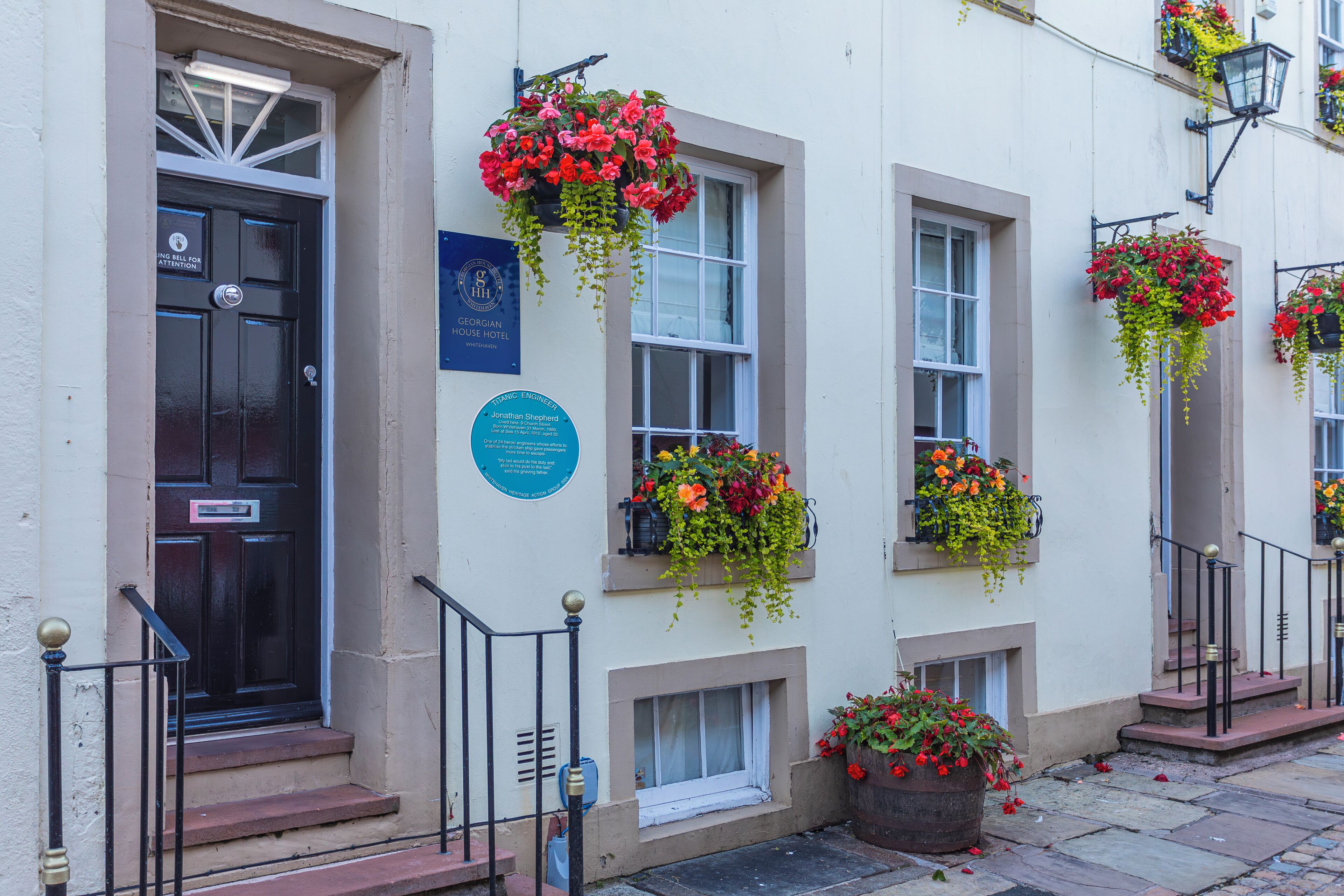 Un edificio con una puerta negra, una placa azul y macetas con flores en los alféizares de las ventanas.