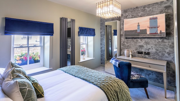 A bedroom with a large bed, a desk, and a chair. There is a window with a view of flowers and a lamp on the desk. - Georgian House Hotel (Whitehaven)
