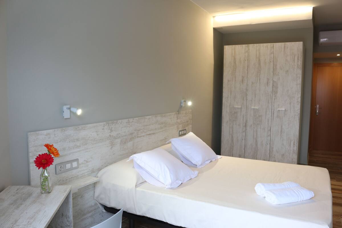 Une chambre d’hôtel avec un lit, une table de chevet, un vase avec des fleurs et une armoire.