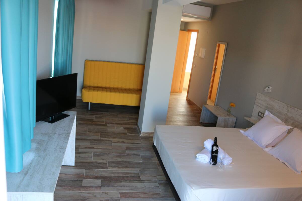 Une chambre d’hôtel avec un lit, une télévision, un canapé et une salle de bain visible au fond.