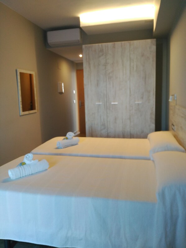A hotel room with two beds, a large mirror, and a wooden wardrobe.