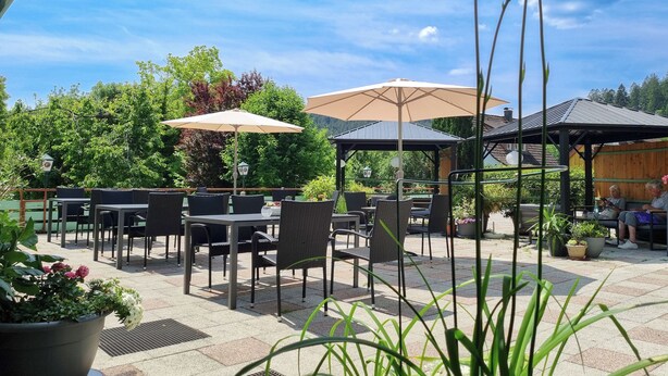 Un espace extérieur aménagé en terrasse, avec des tables, des chaises, des parasols et des plantes en pot.