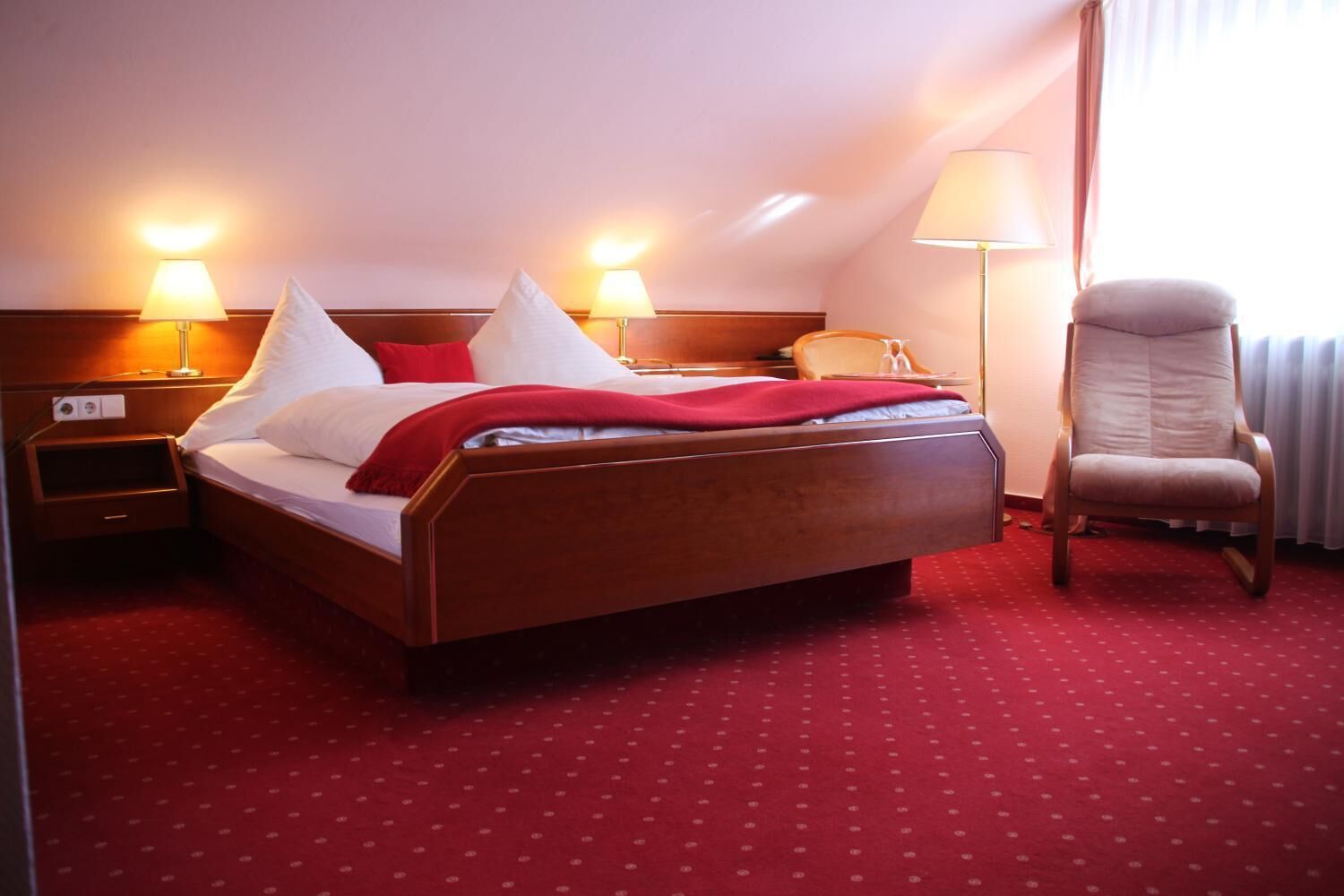Habitación de hotel con una cama grande, dos lámparas de noche, una silla y una alfombra roja.