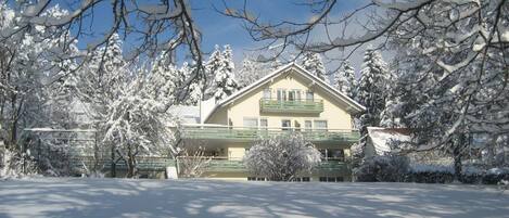 Una casa de dos pisos con balcón, rodeada de árboles cubiertos de nieve.