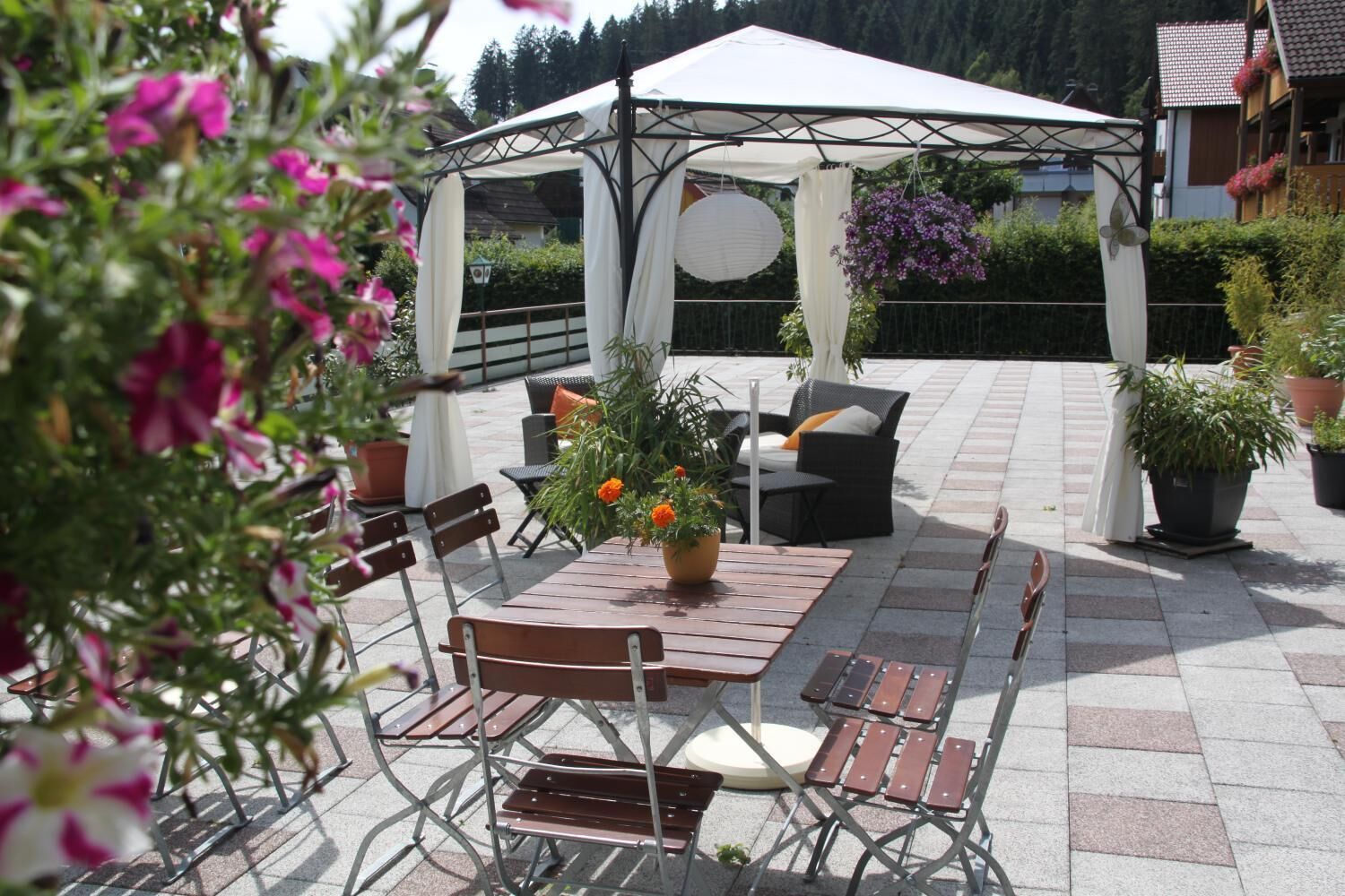 An outdoor patio with a covered seating area, a table with chairs, and potted plants.