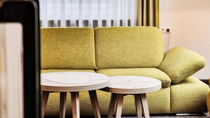 Un canapé vert avec deux petites tables rondes en bois devant.