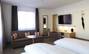 Une chambre d’hôtel avec un canapé, un bureau, une télévision et deux lits.