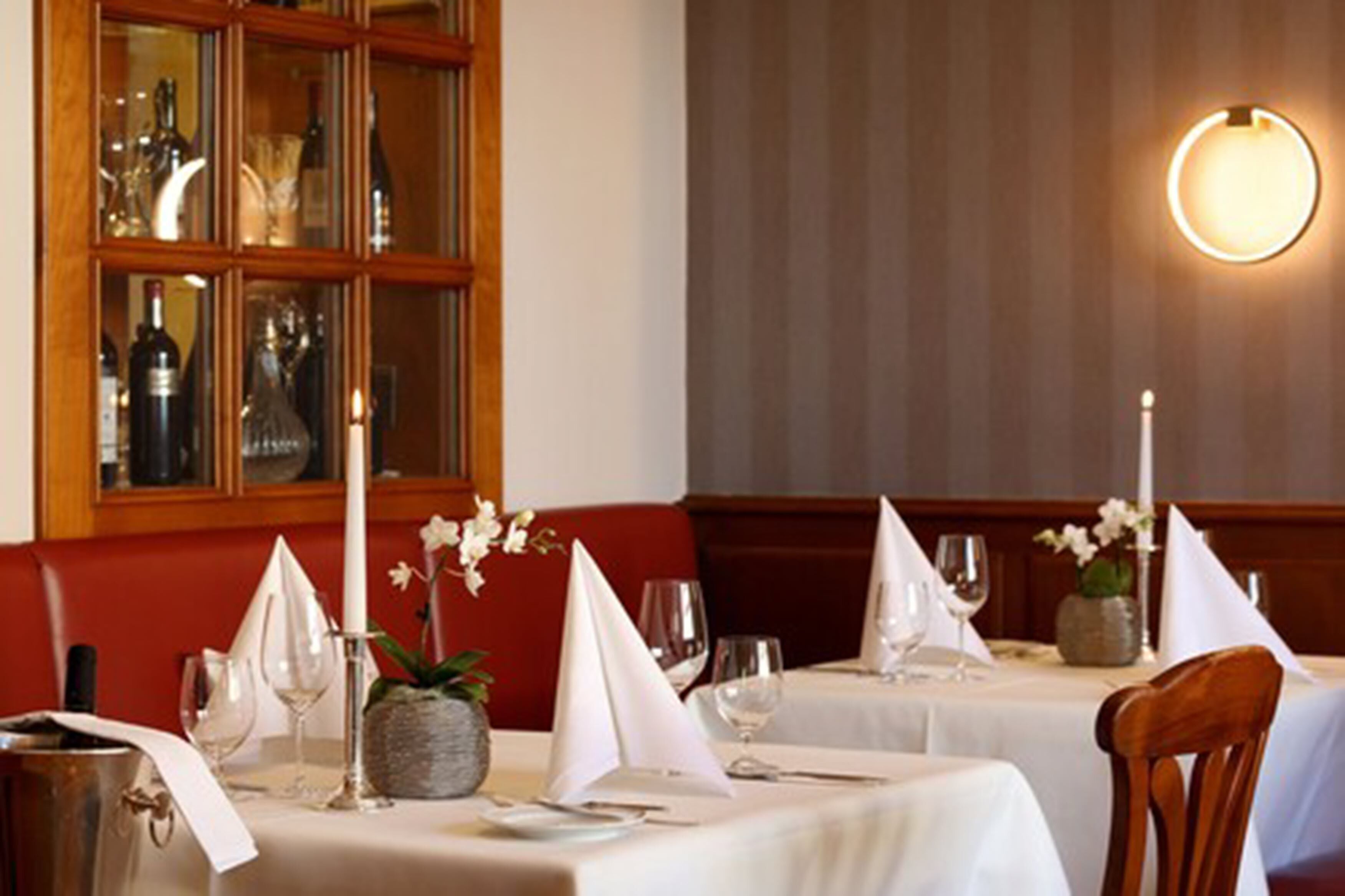 Un restaurant où les tables sont dressées pour le dîner, avec des nappes blanches, des bougies et des arrangements floraux en guise de décoration.