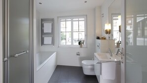 Un baño moderno con bañera, inodoro y lavamanos. Hay una ventana que proporciona luz natural y vistas al exterior.